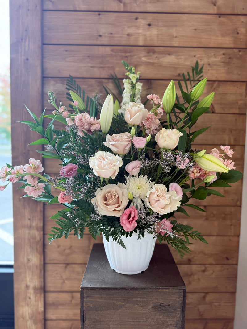 White and pale pink flowers with lilies and greenery arranged in a white vase.