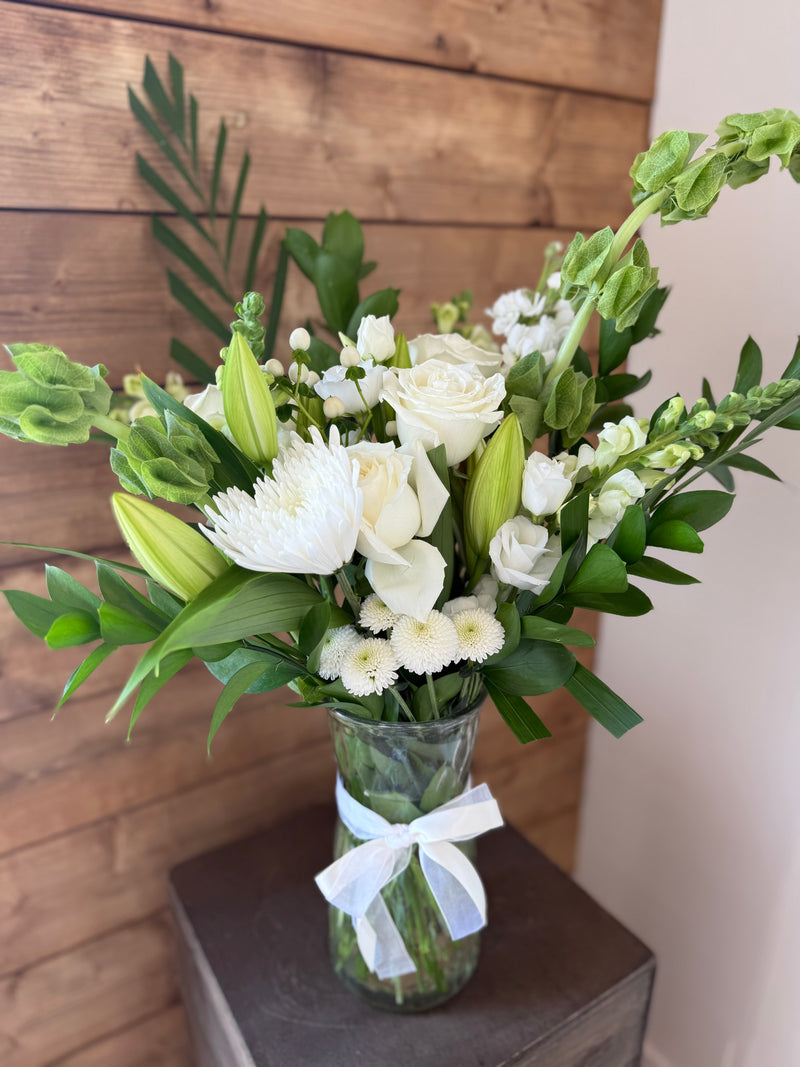 Fresh whites and greens arrangement displayed in a clear vase accented with a white bow.