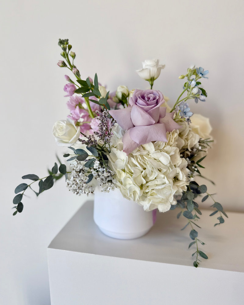 Centrepiece with a mix of white and lavender flowers in a white circular vase.