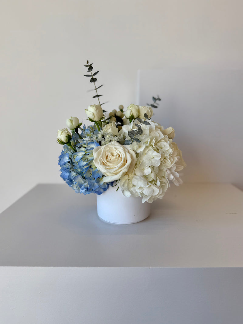 Floral arrangement with blue hydrangeas and white roses in a white vase.