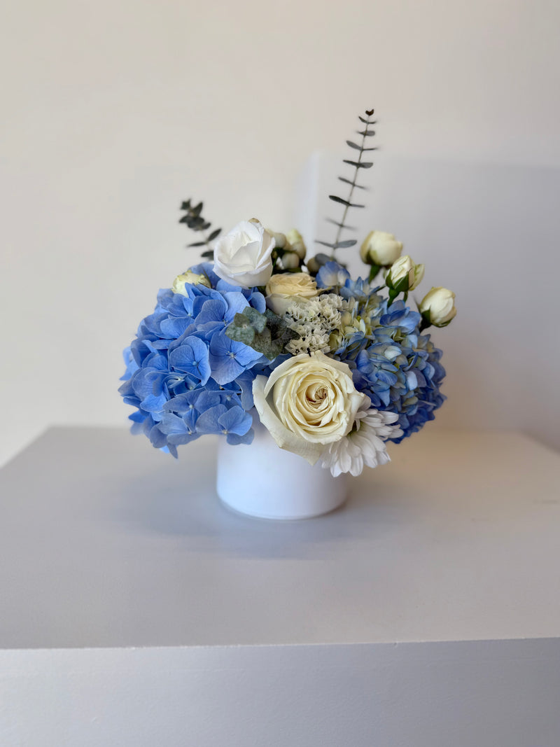 Floral arrangement with blue hydrangeas and white roses in a white vase.
