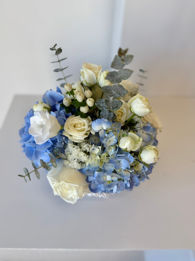 Floral arrangement with blue hydrangeas and white roses in a white vase.