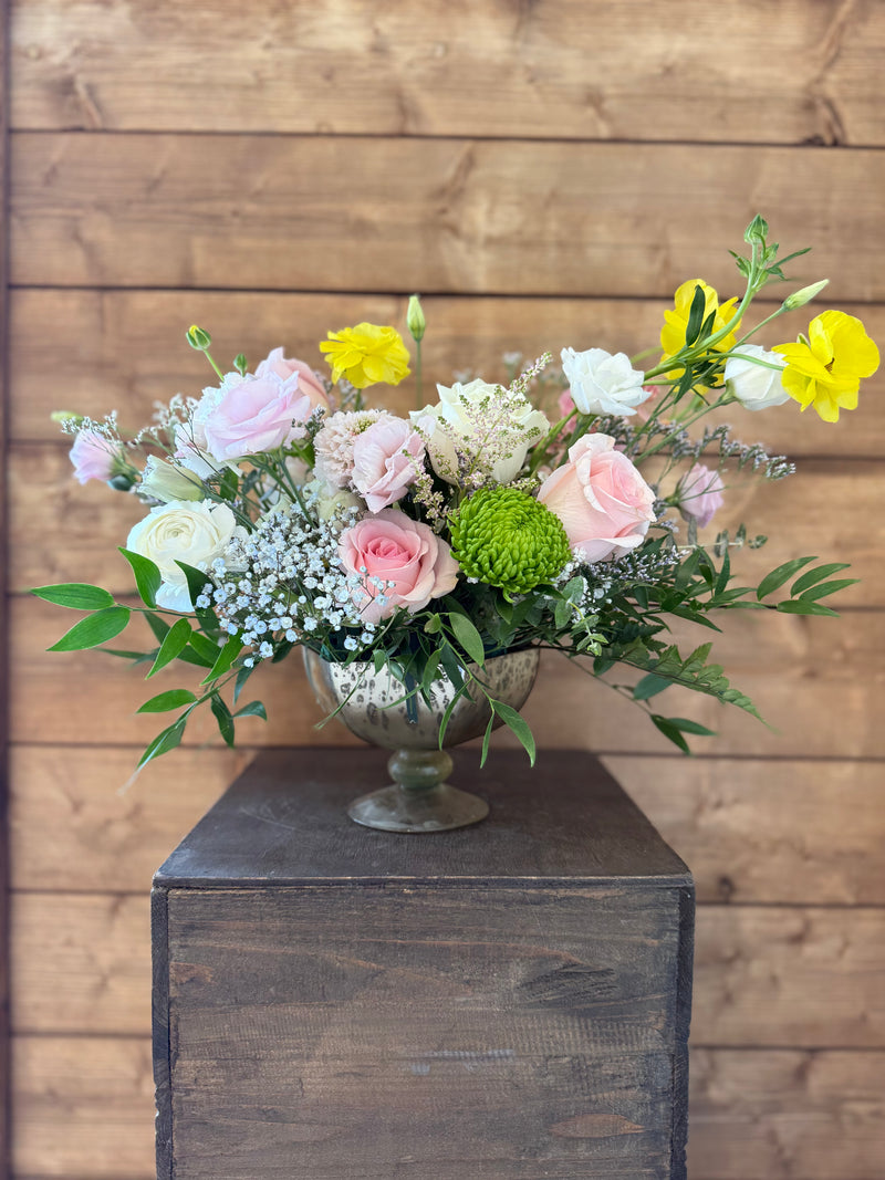 Mix of white, blush, and sunny yellow blooms with fresh greenery in a silver chalice vase.