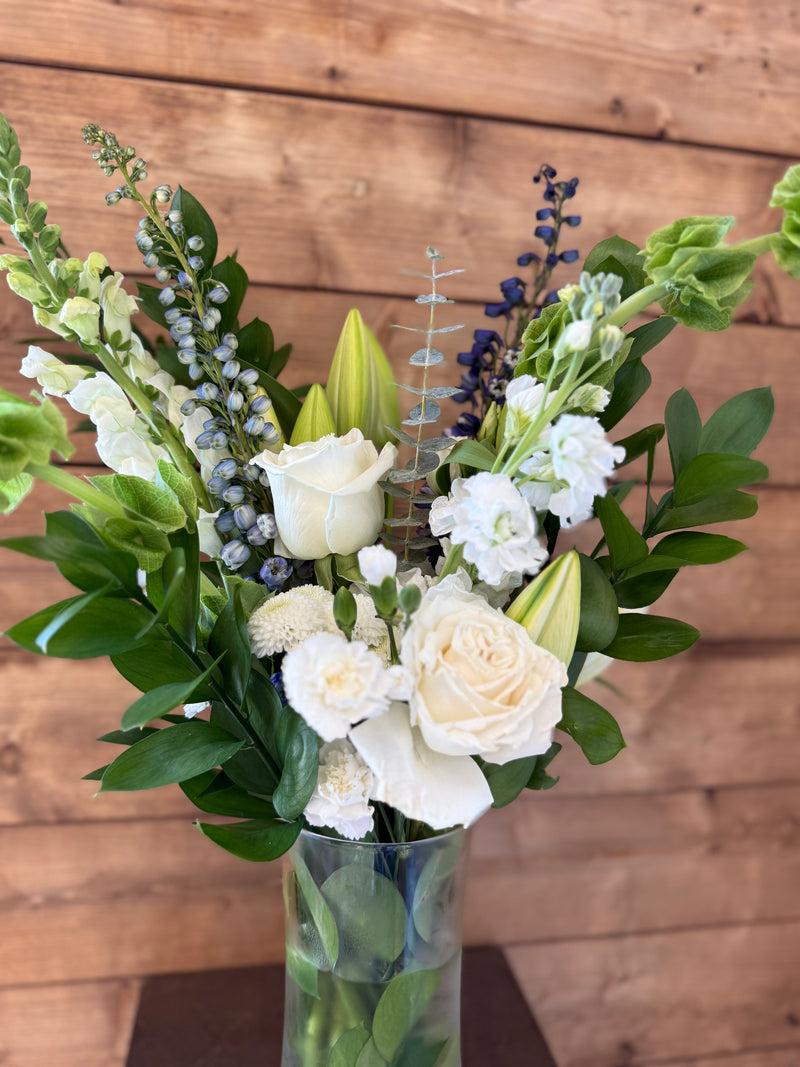 Close-up of large white and green flowers with blue accents in a clear glass vase.