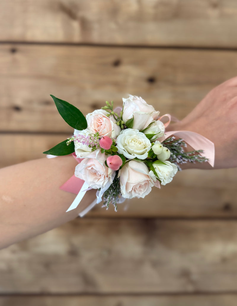 Elegant wrist corsage featuring light pink and white mini roses tied with a satin ribbon.