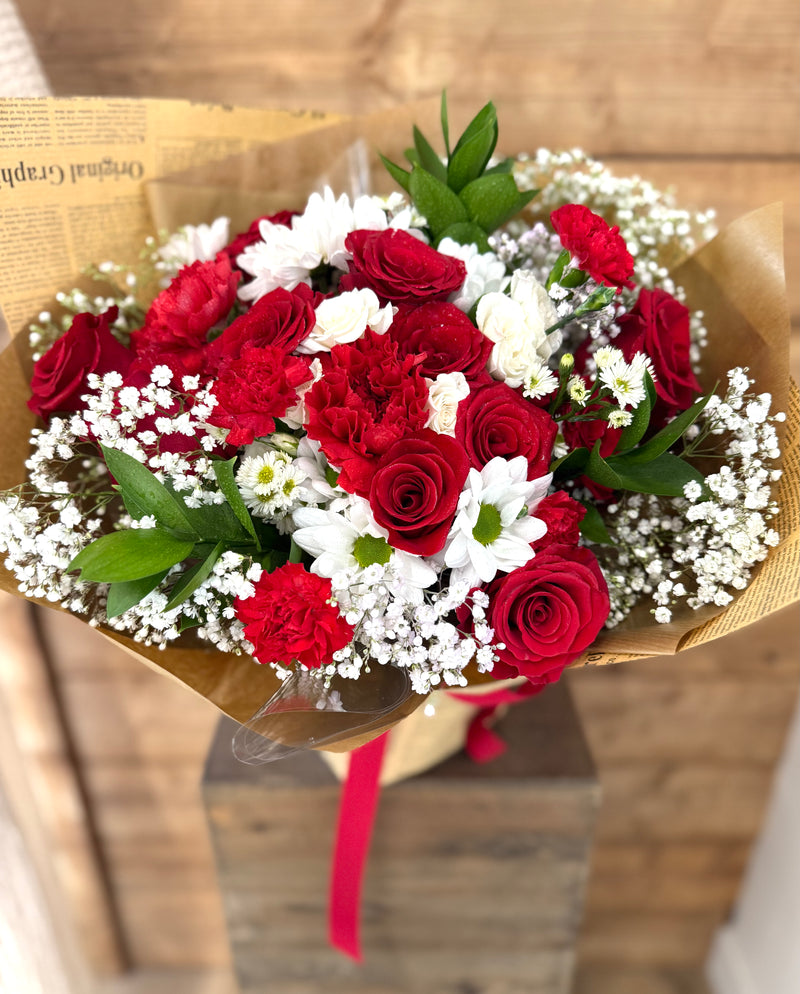 Mixed red and white floral bouquet wrapped in newspaper-style brown paper with a red ribbon.