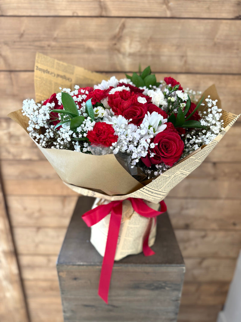Mixed red and white floral bouquet wrapped in newspaper-style brown paper with a red ribbon.