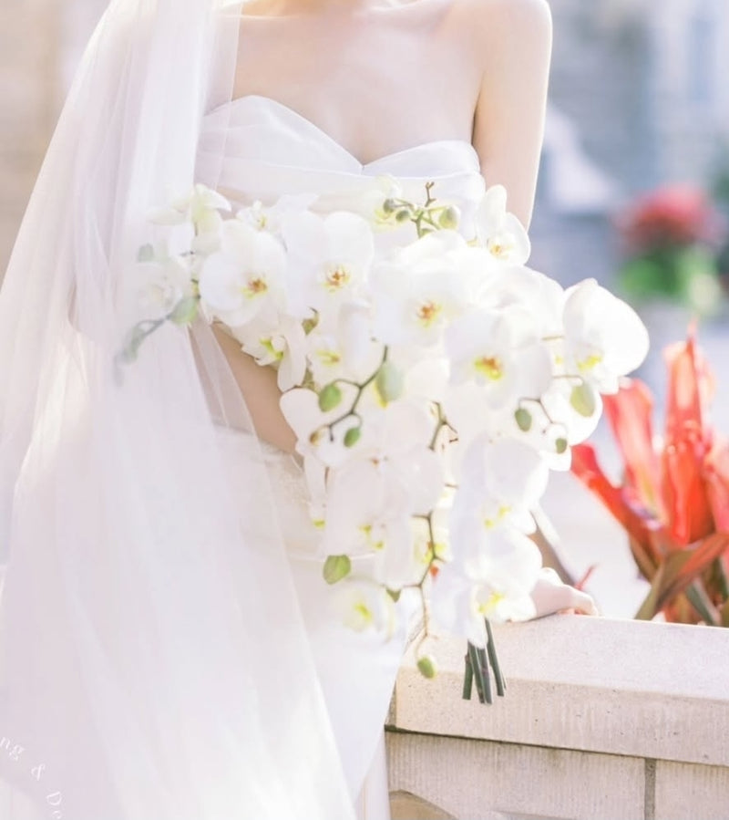 Luxurious cascading white orchid bridal bouquet tied with a white ribbon.