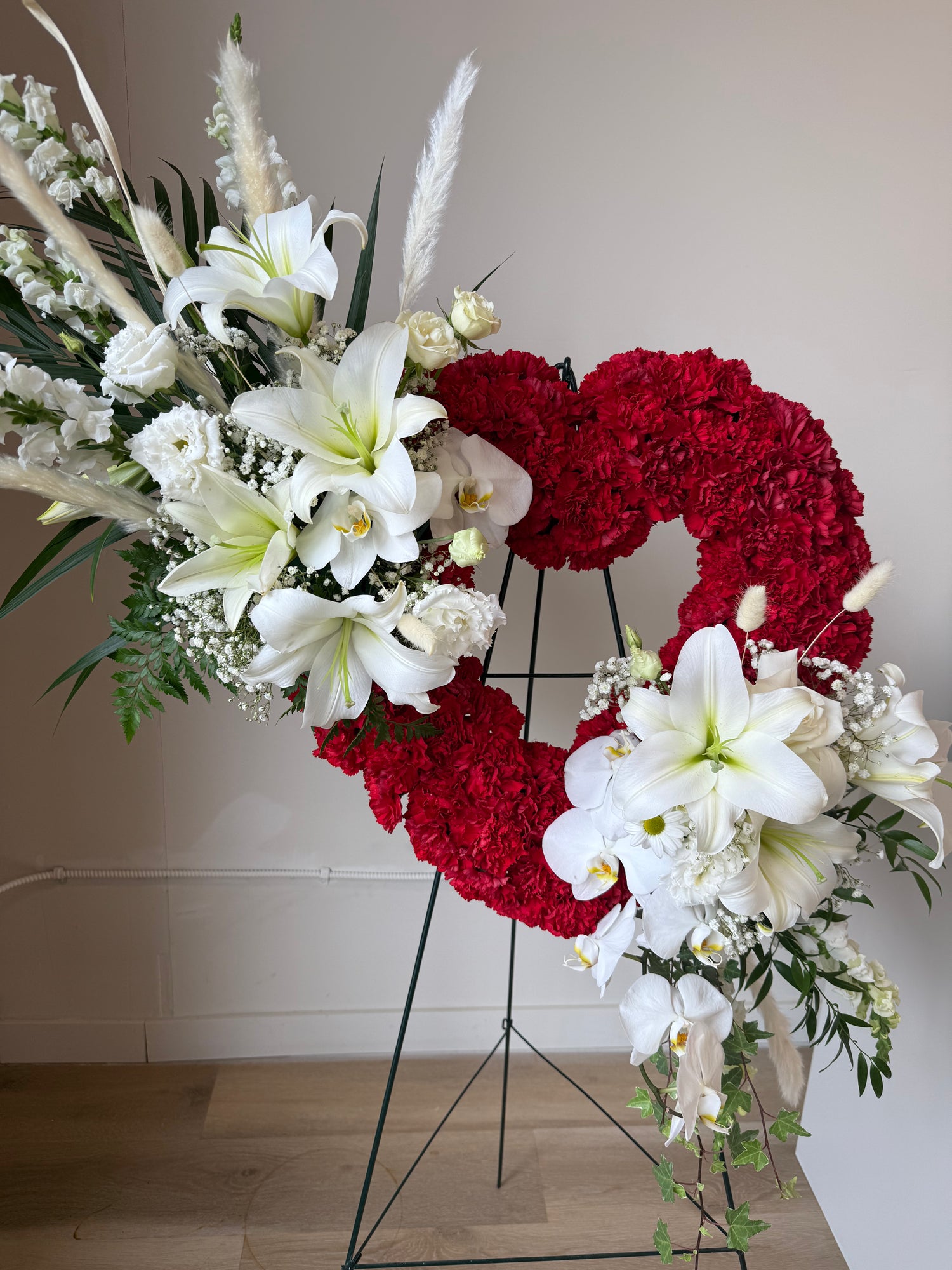 Red heart-shaped wreath with 2 bunches of greenery with white lilies, white orchids and white fillers