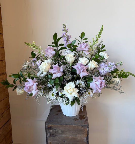 White and lavender roses, white chrysanthemums and filler flowers in a white vase for funeral or memorial service