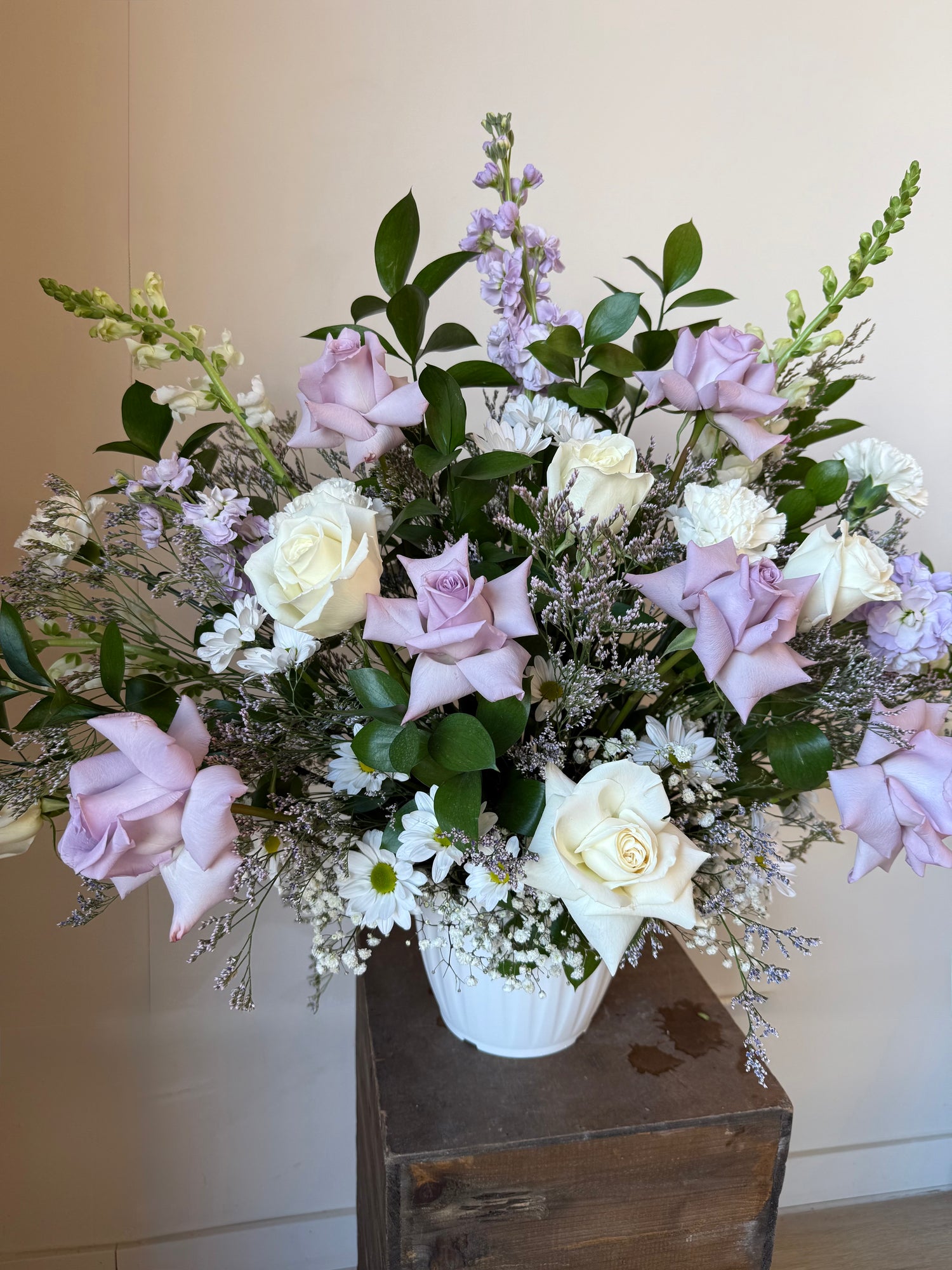 White and lavender roses, white chrysanthemums and filler flowers in a white vase for funeral or memorial service