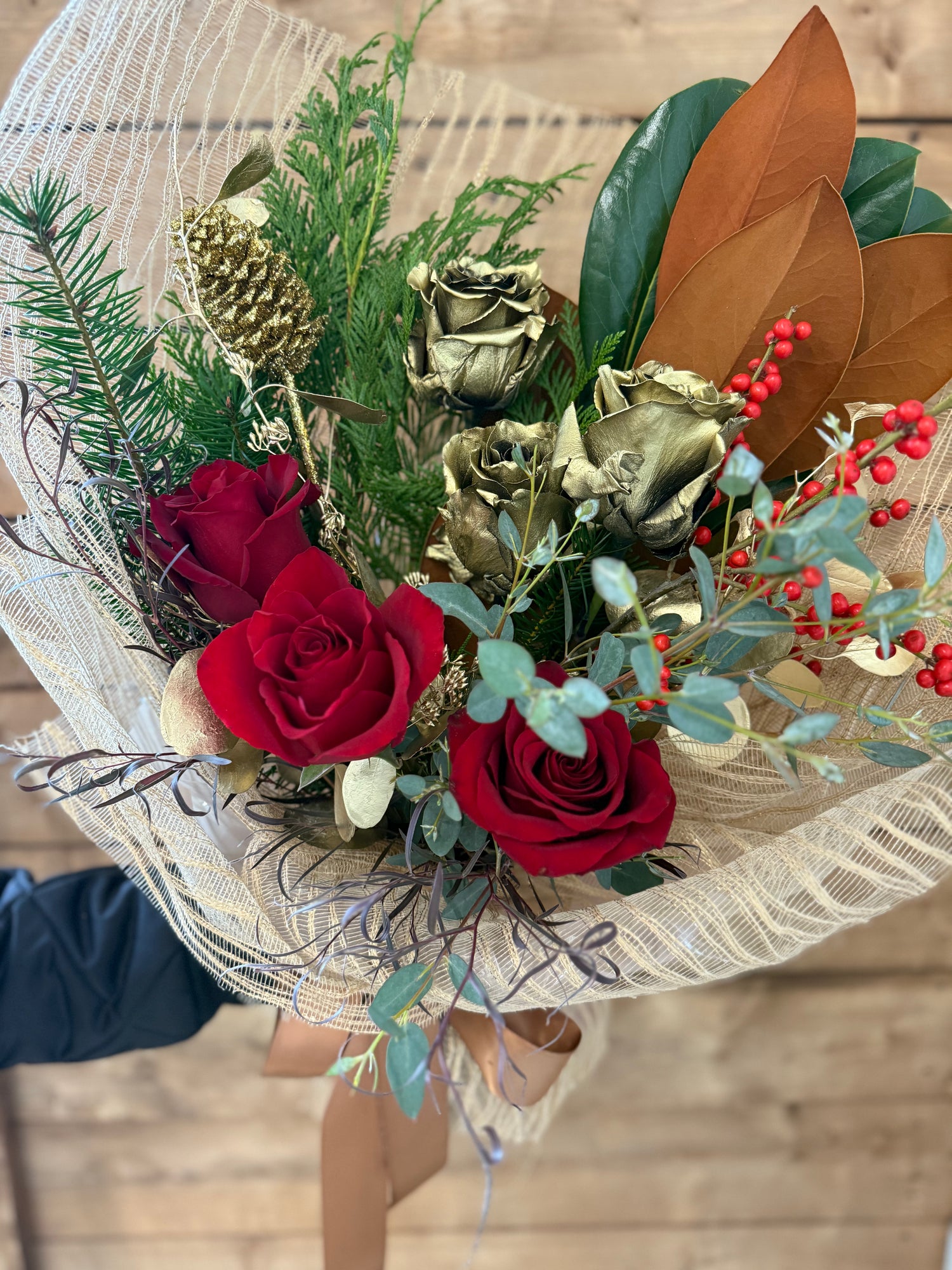 Bouquet of red and gold roses with winter foliage wrapped in a gold net.