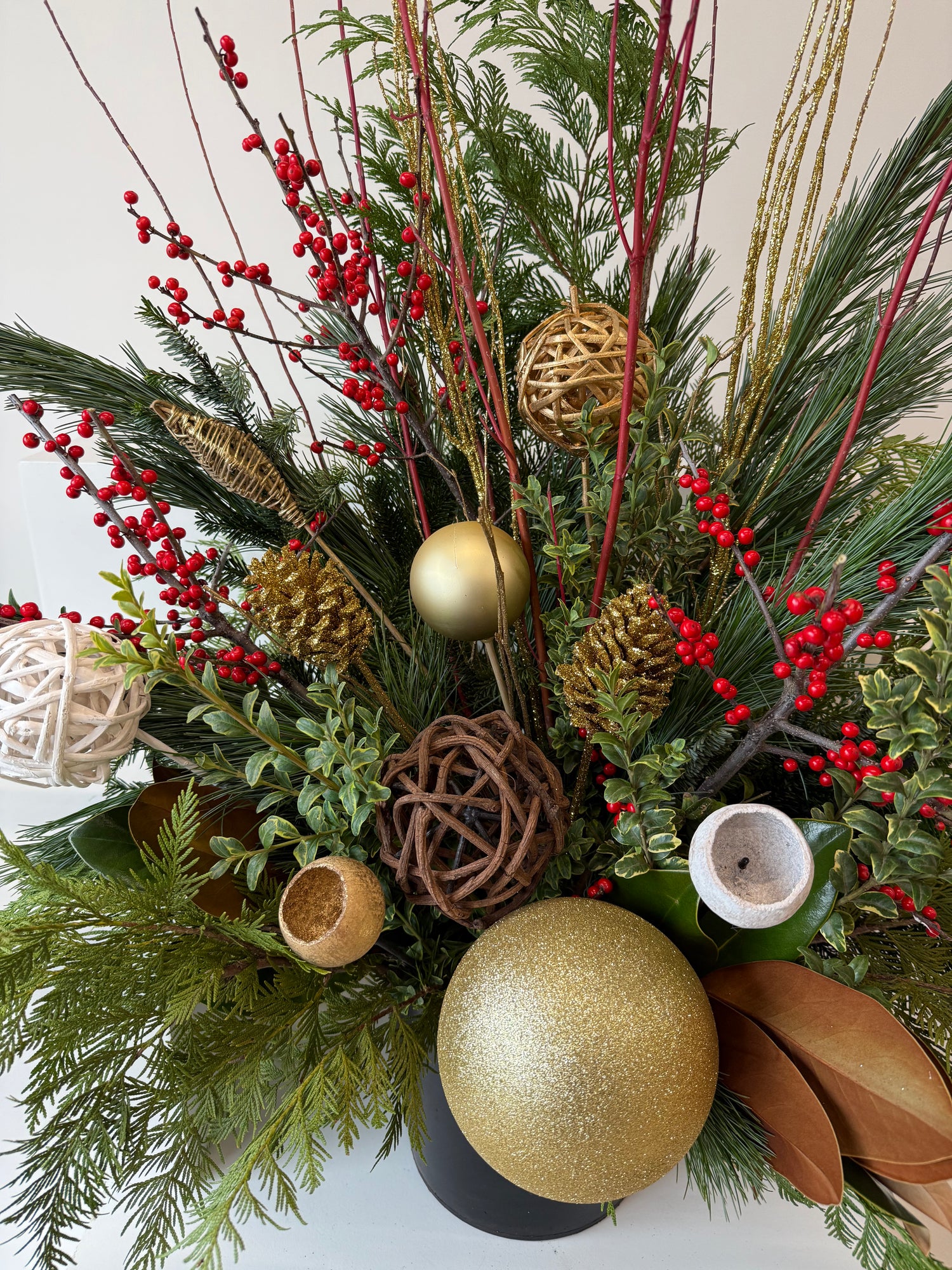 Winter planter decorated with ilex, sparkling gold accents, and verdant evergreens.