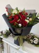 Red rose and a hint of white roses bouquet nestled among fresh winter greens shimmer with gold accents.