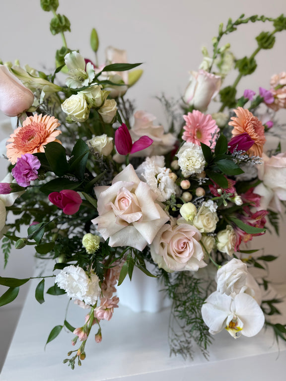 Floral arrangement peach and blush blooms arranged in a white vase.