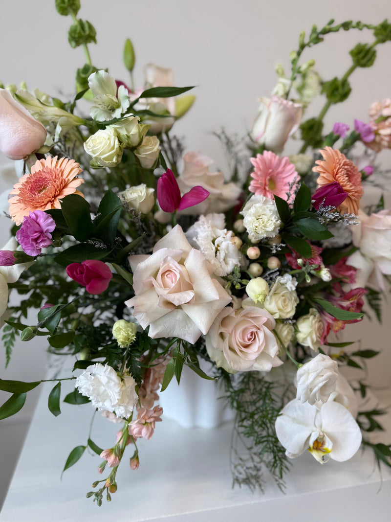 Floral arrangement peach and blush blooms arranged in a white vase.