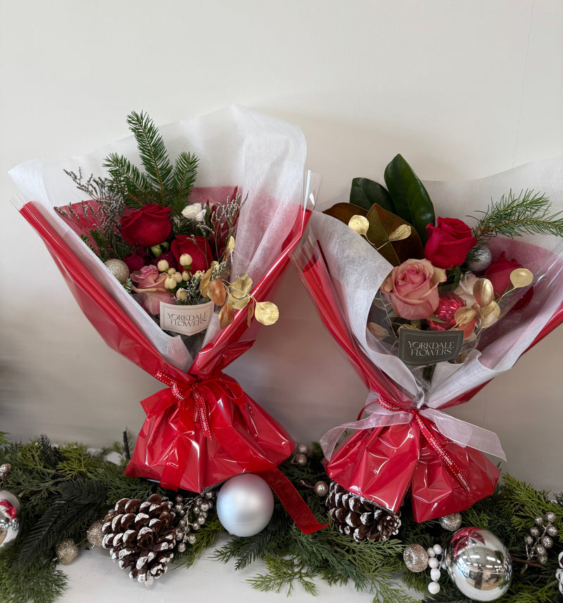 Bouquet of mix red blooms and winter foliage, finished with a delicate gold accent for a warm holiday touch.