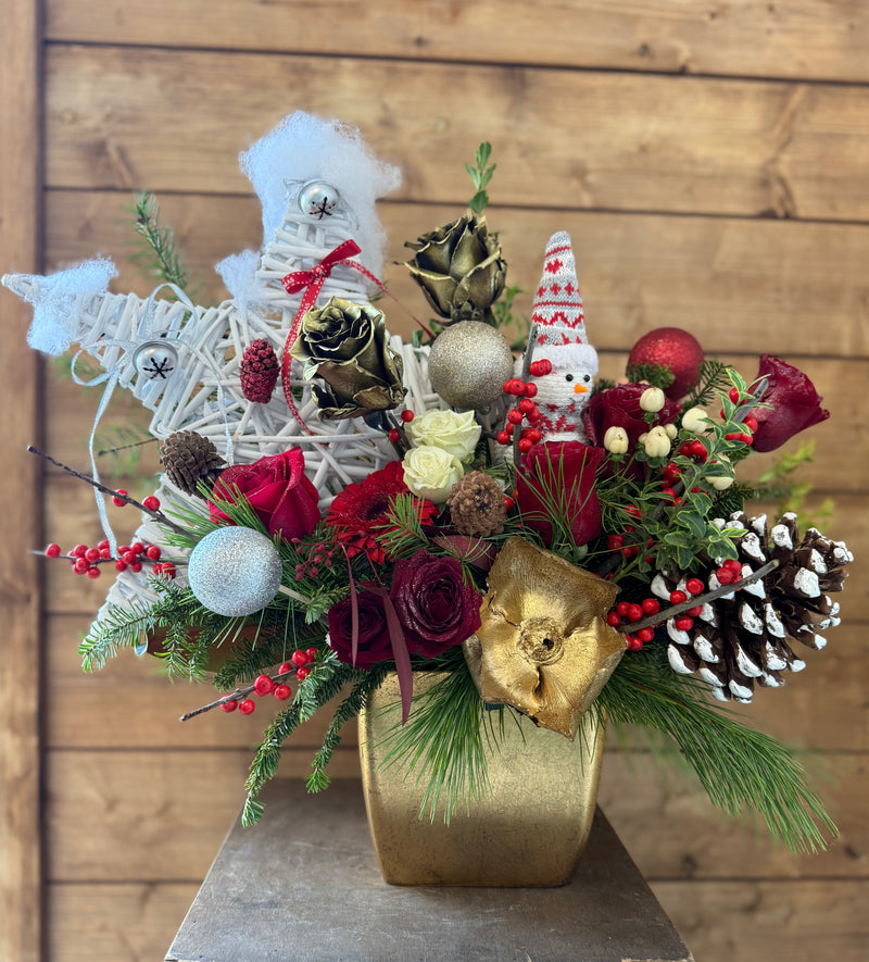 Decorative floral arrangement with Christmas-themed elements in a gold vase.
