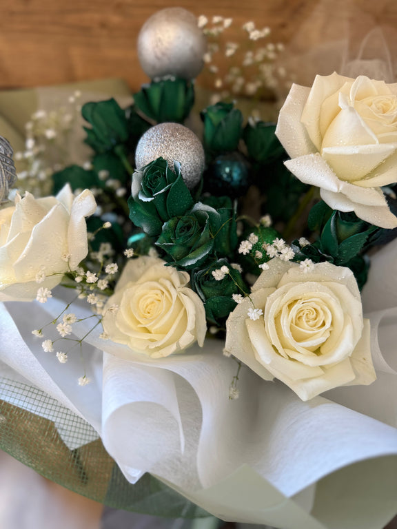 Handcrafted Christmas bouquet of white and green roses with holiday ornaments, wrapped in green paper and green net—perfect for festive gifting.