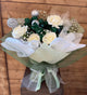 Handcrafted Christmas bouquet of white and green roses with holiday ornaments, wrapped in green paper and green net—perfect for festive gifting.