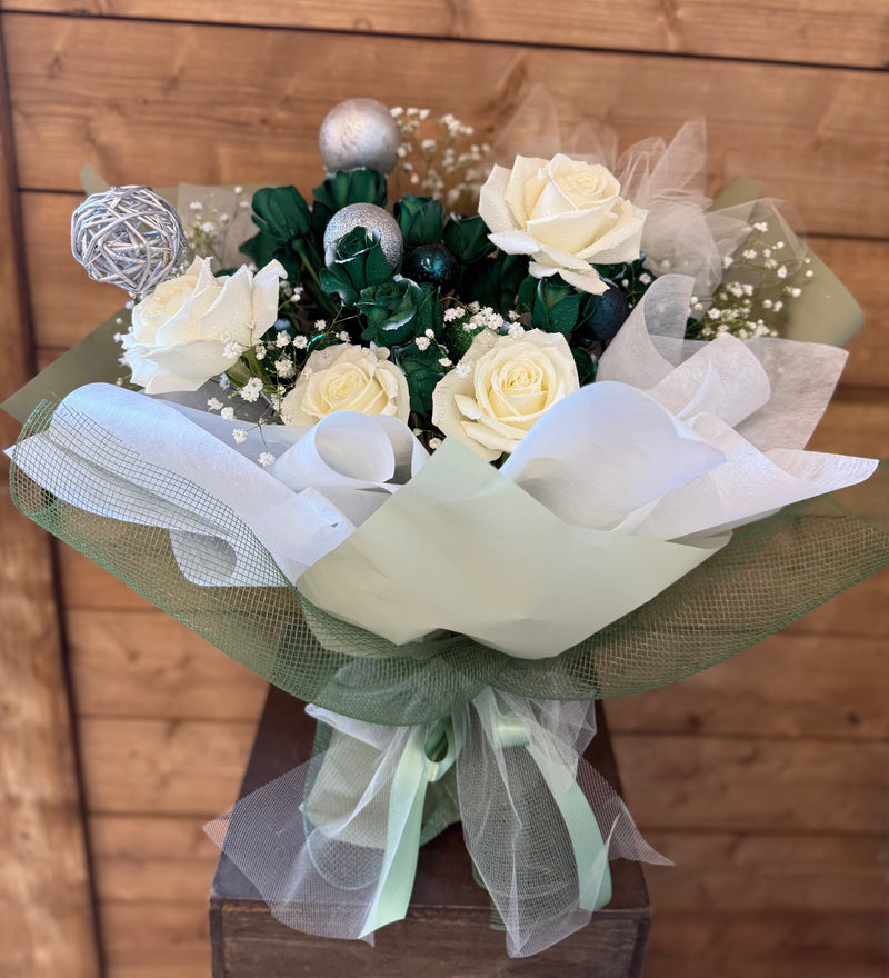 Handcrafted Christmas bouquet of white and green roses with holiday ornaments, wrapped in green paper and green net—perfect for festive gifting.