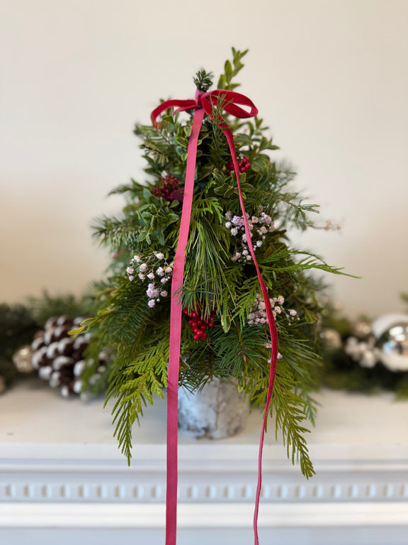 Handcrafted small Christmas tree arrangement featuring festive greenery and red ribbon accents—perfect for holiday décor.