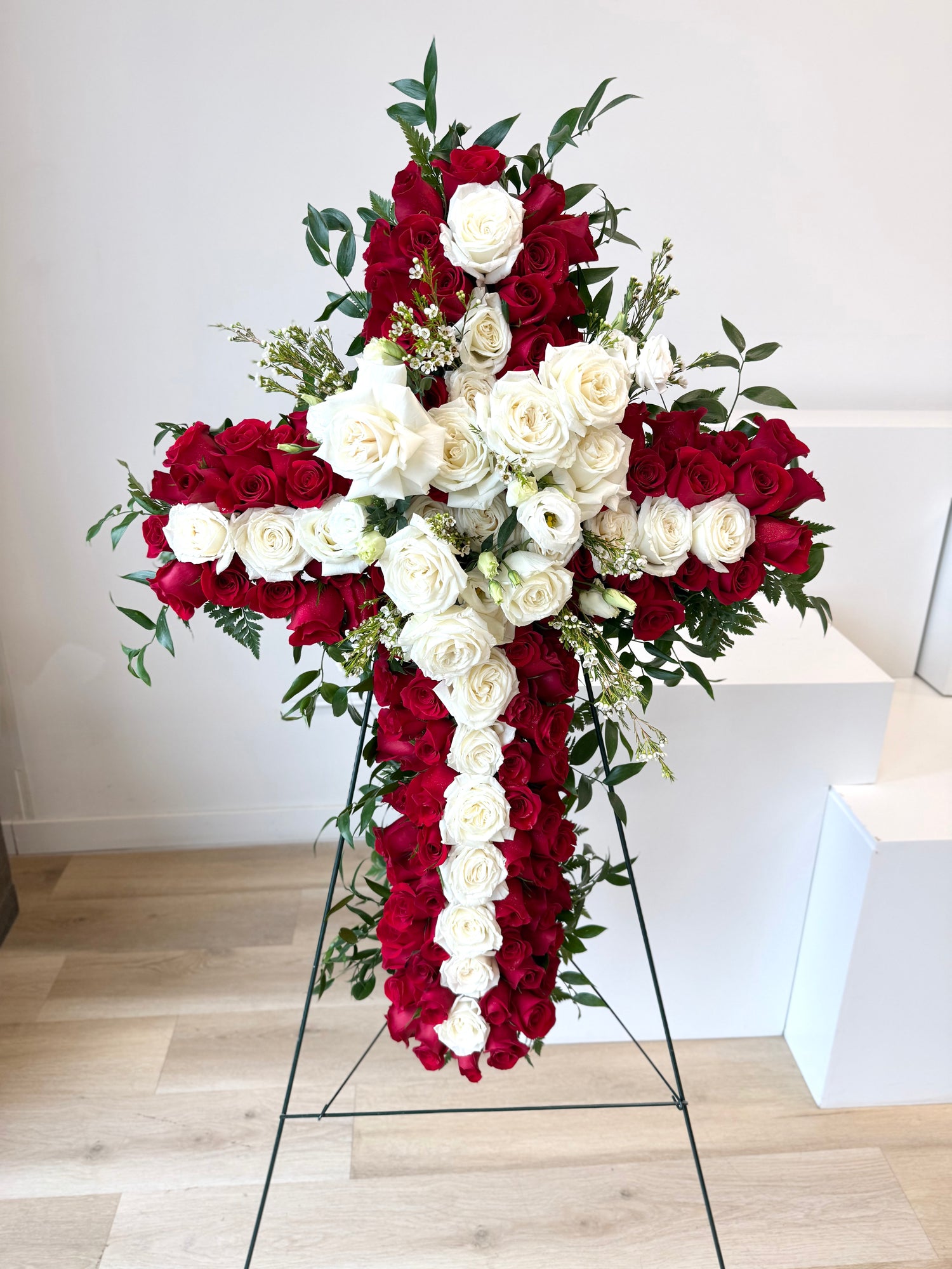 Floral cross arrangement with red and white roses, greenery