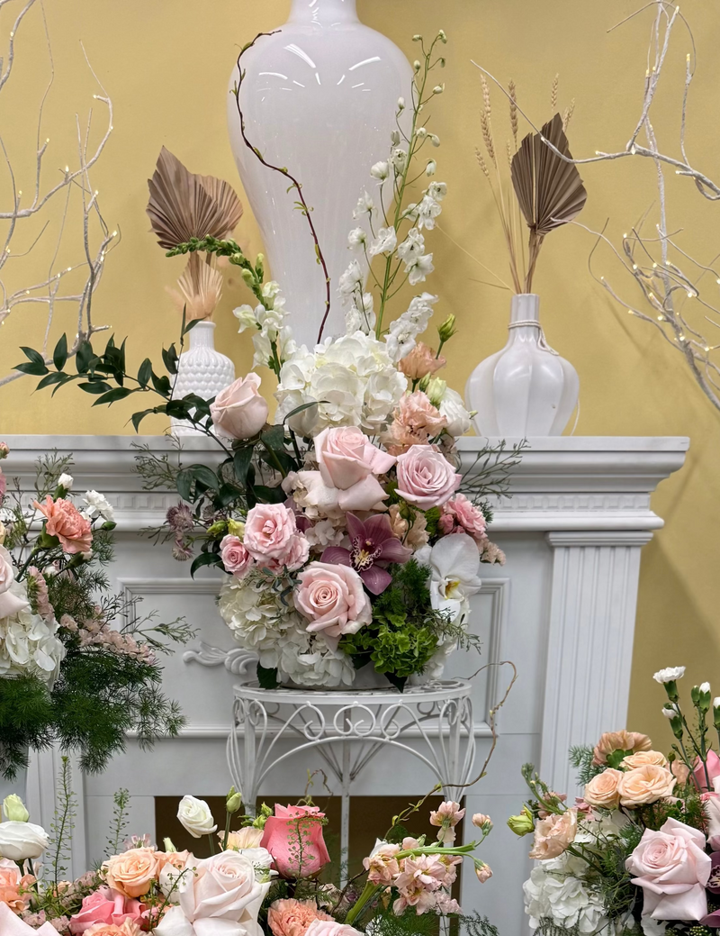 Arrangement of light pink and peach blooms nestled among fresh, textural greenery.
