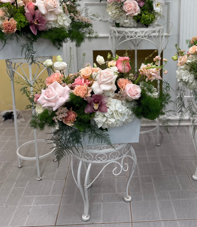 Centrepiece with soft pink and peach flowers and textured greenery in a rectangular withe vase.